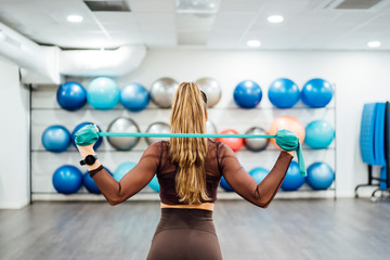 Beautiful woman in gym performing exercises with elastic bands.