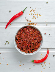 Bowl with red Moroccan harissa and fresh red chili peppers on white background