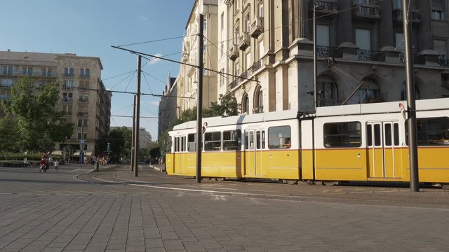 Tram crossing in front of Budapest Parliament, with people walking around. Dolly shot