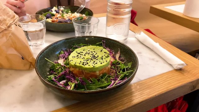 Zoom out from fresh delicious salmon tartar with green fresh guacamole and white and green seeds - rucola and red white cabbage