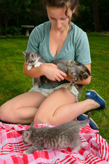 Teenage girl holding kittens playing outdoors with blanket on a grass lawn