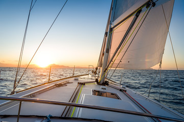 Sailing yacht navigationg to the sun rising on the horizon.. Mediterranean sea, Italy.