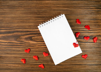 Notepad with a blank sheet on a wooden background with hearts. Love letter.