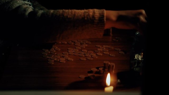 An elderly man counts coins on the table. A candle is burning. The concept of poverty and helplessness. Close - up of the room.