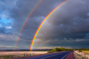 After an evening summer showers. A bright rainbow stands over the highway. Trucks and passenger cars go on the wet asphalt. Real photo - montage or graphic software was not used.