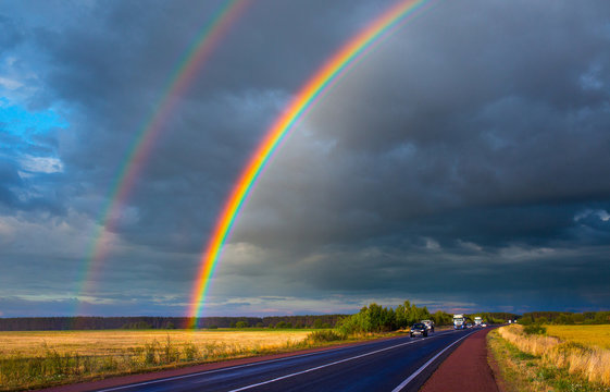 After an evening summer showers. A bright rainbow stands over the highway. Trucks and passenger cars go on the wet asphalt. Real photo - montage or graphic software was not used.