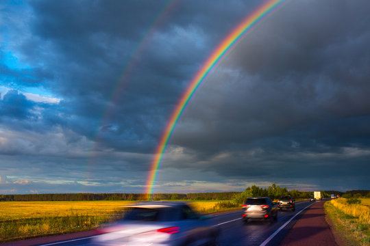 After an evening summer showers. A bright rainbow stands over the highway. Trucks and passenger cars go on the wet asphalt. Real photo - montage or graphic software was not used.