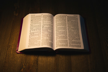 Open Holy Bible over a wooden table at night