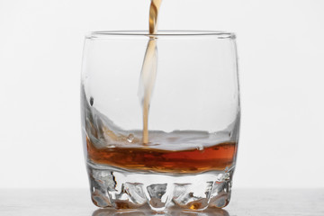 Process of filling glass by whiskey with ice on white background