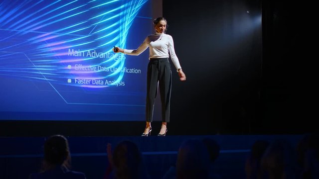 On Stage: Inspirational Female Speaker, Talking about Happiness, Self, Success, Efficiency, Health, and How to Be More Productive. Tech Industry Business Conference Auditorium Hall full off People