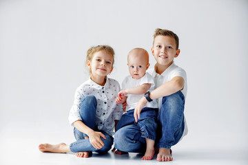 Happy sisters and brother are sitting on the floor on a white background. Two teens and a baby 1...