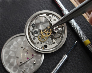 close up of watchmaker repairing old mechanical watch caliber taking small gear with tweezers