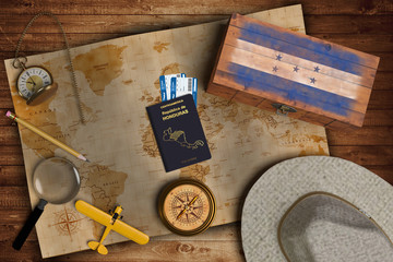 Top view of traveling gadgets, vintage map, magnify glass, hat and airplane model on the wood table background. On center, official passport of Honduras and your flag.