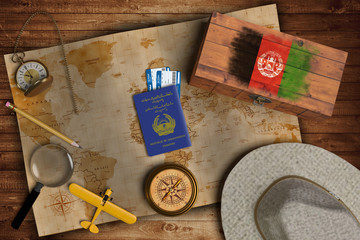 Top view of traveling gadgets, vintage map, magnify glass, hat and airplane model on the wood table background. On center, official passport of Afghanistan and your flag.