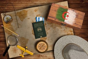Naklejka premium Top view of traveling gadgets, vintage map, magnify glass, hat and airplane model on the wood table background. On center, official passport of Algeria and your flag.