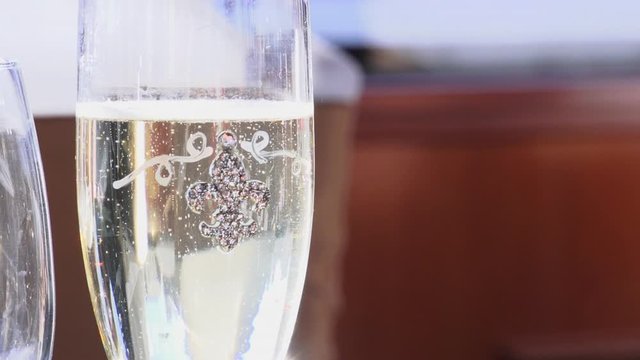 A glamorous sun lit slow motion shot of bubbles in a fleur de lis champagne glass. Close up with a defocussed background. Slow motion.