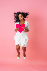 Love is in the air, full body portrait of a young happy woman holding heart and jumping up