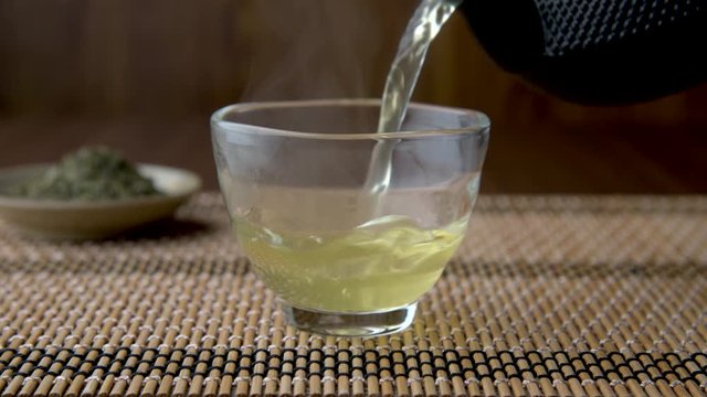 Hot Japanese green tea in glass cup with teapot and leaf