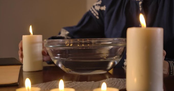Side view close-up of unrecognizable Caucasian old woman moving candle around water in plate. Mature female fortune teller predicting fate. Cinema 4k ProRes HQ.
