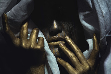 Creative closeup portrait of female face covered with colden paint wrapped in rough white fabric