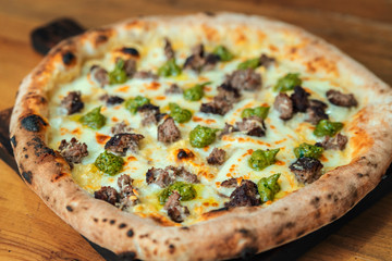 Freshly baked pizza with cheese, sauce and meat on a wooden table close up