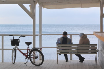 an elderly man and woman admire the winter sea sitting on a bench in a cafe