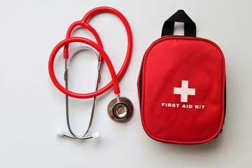 Red first aid kit with a stethoscope  on a pale blue background.