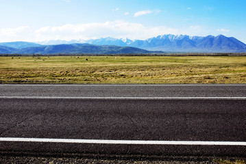 asphalt road along a green valley on a background of snowy mountains