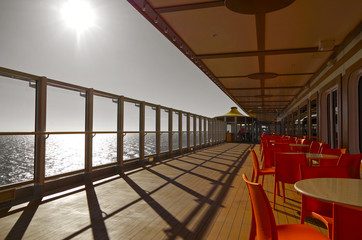 Relaxing on outdoor promenade with sun umbrellas and deck chairs with ocean views on luxury cruise...