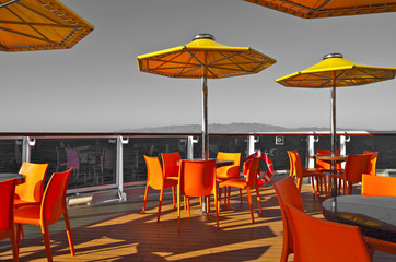 Relaxing on outdoor promenade with sun umbrellas and deck chairs with ocean views on luxury cruise...