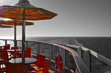 Relaxing on outdoor promenade with sun umbrellas and deck chairs with ocean views on luxury cruise...