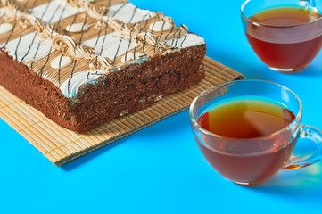 One whole checkered rectangular cake near two full glass cups of tea lies on blue table on party. Celebration concept. Close-up