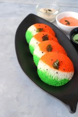 Tiranga Idli or Tricolor Idly cooked in  Indian National Flag colors - saffron or orange, white and green. Served with tiranga chutney. Concept for Indian Independence or Republic day greeting card.