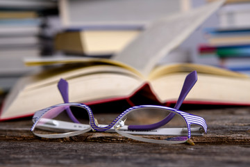 book and reading glasses in front of piles of different books