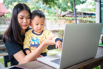 Smart young asian mom hold baby boy use laptop computer in cafe