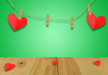 A Valentine's day concept.A red heart shaped card attached to a wooden clip Hanging with hemp rope on pastel  green.Valentine's Day background