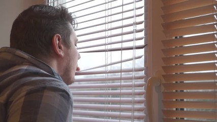 curious man looks out the window through the blinds