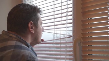 curious man looks out the window through the blinds