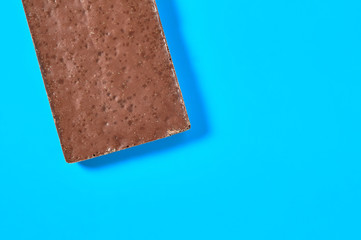 Single whole dark porous chocolate bar lies on blue table on kitchen. Space for text. Top view
