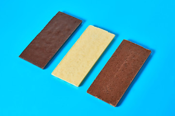 Row of three various whole porous chocolate bars lies on blue table on kitchen. Close-up