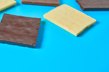 Scattered pieces of various whole porous chocolate bars lies on blue table on kitchen. Space for text