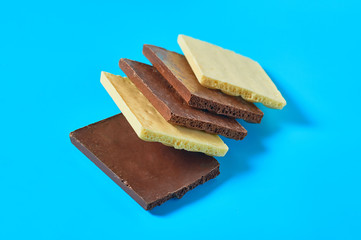 Heap of halves various whole porous chocolate bars lies on blue table on kitchen. Close-up