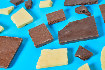Scattered pieces of various whole porous chocolate bars lies on blue table on kitchen. Close-up