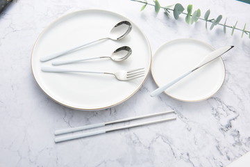 Chopsticks, spoons, knives and forks are arranged on ceramic plates