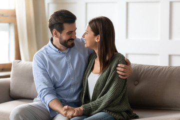 Happy couple sit on couch hugging reunited after fight