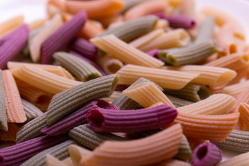 Tri-color penne pasta. Tomato, spinach and wheat pastas. Multicolored pasta of red, yellow and green color, organic square background.