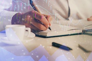 Double exposure of man's hands writing notes of stock market with forex chart.