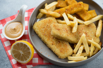 Roasted breaded fish fillet with french fries and lemon in a grey plate, close-up, selective focus