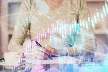 Hand taking notes in notepad. Forex chart holograms in front. Concept of research. Double exposure