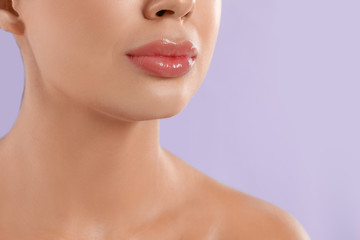 Young woman with beautiful full lips on lilac background, closeup